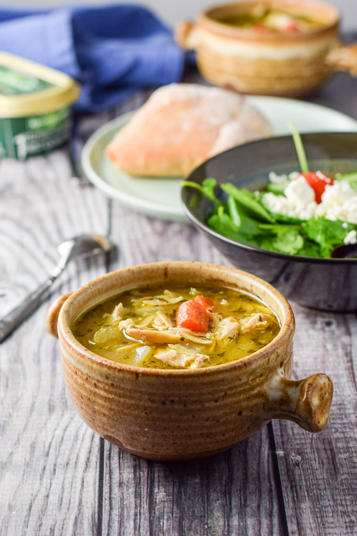 A spoon beside a crock of soup with another in the back