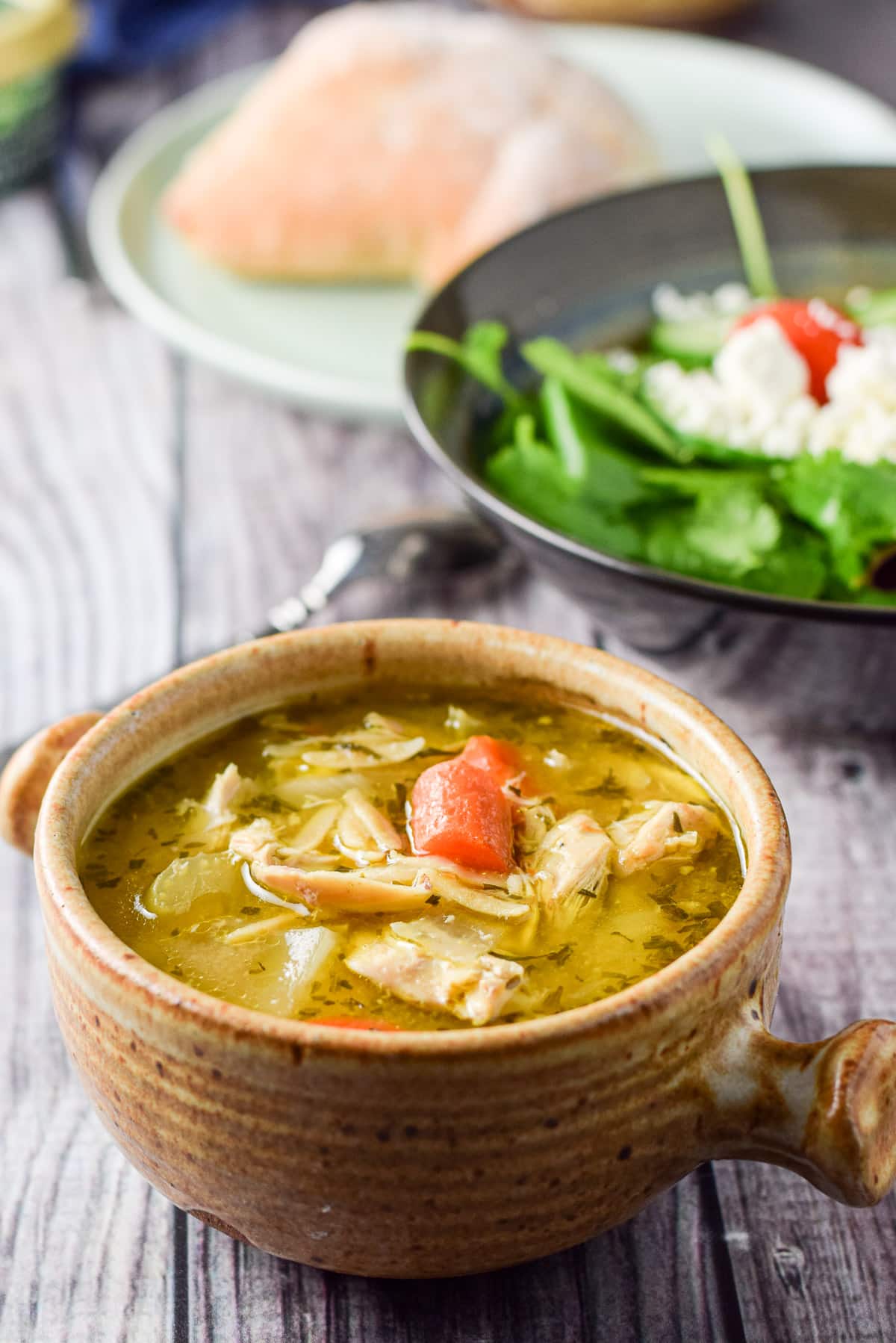 A close up of carrots floating in a chicken soup with a salad in the back