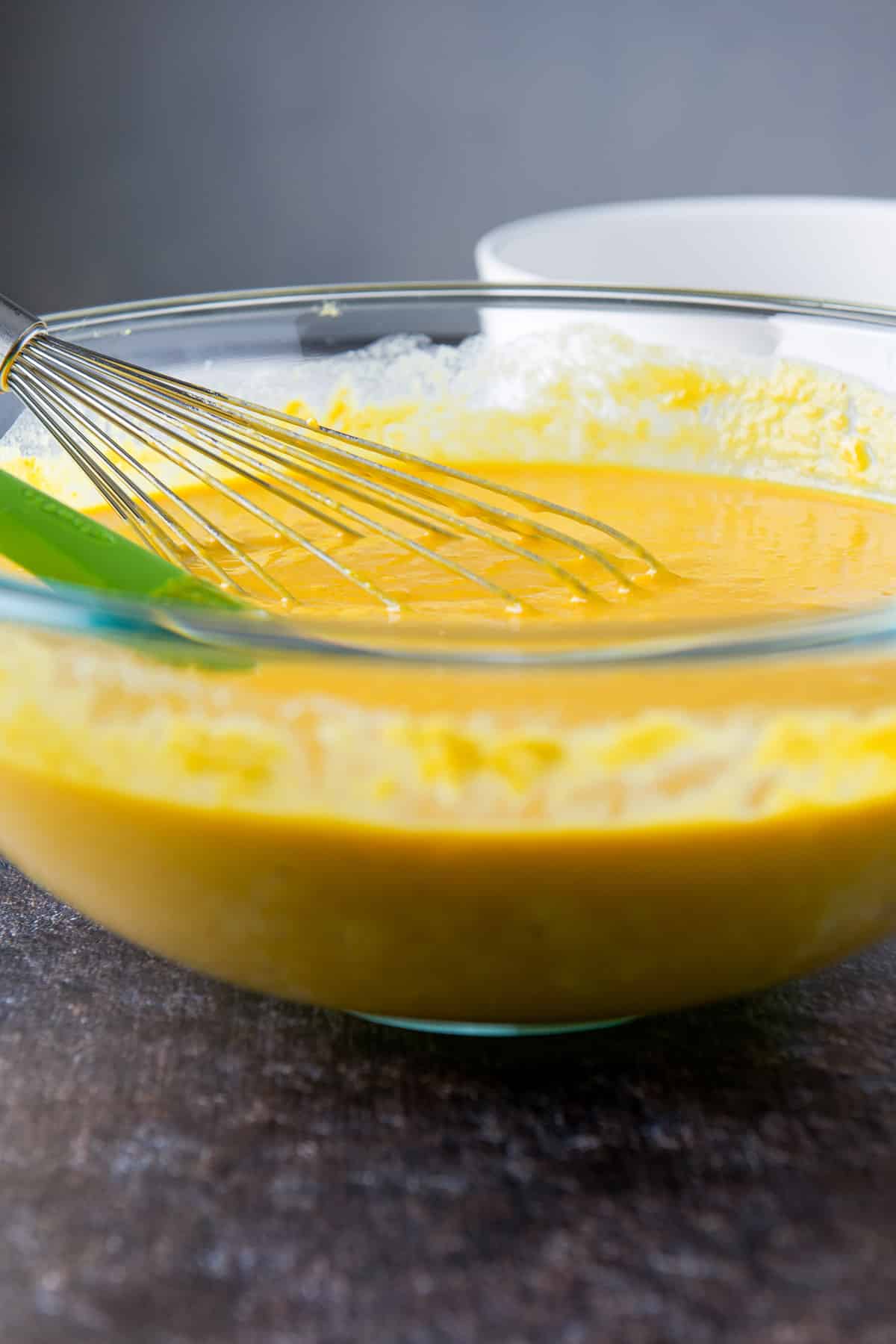The glass bowl with the souffle ingredients mixed together with a spatula and whisk
