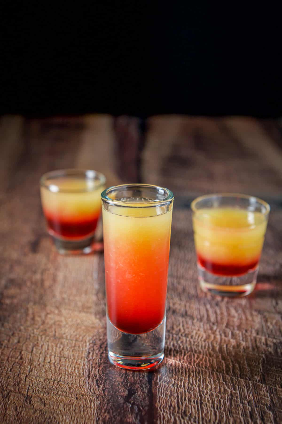 The tall glass filled with the layered shot in front of the others showing the difference of the shot in the glasses