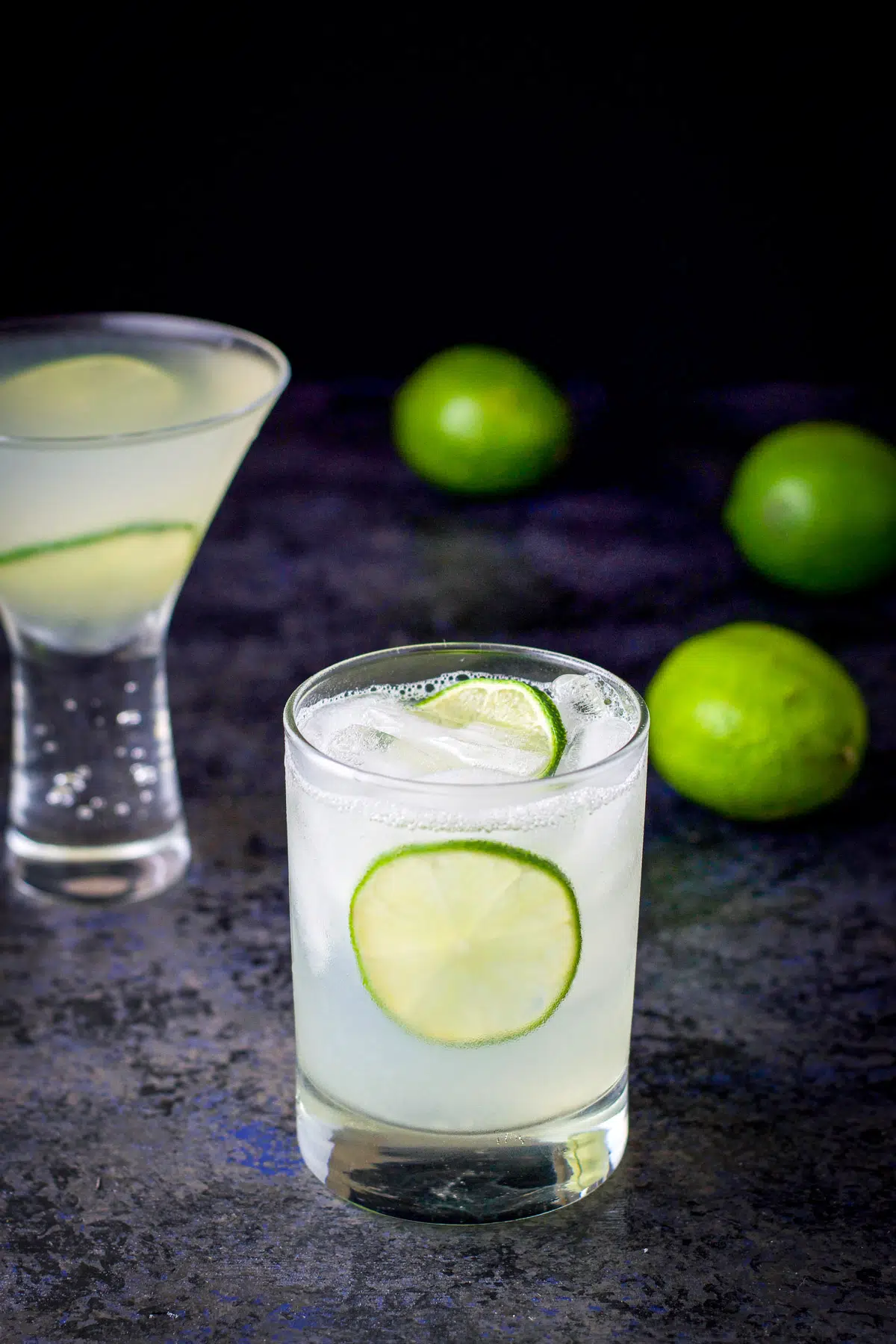 Two lime wheels floating in the gimlet with limes on the table