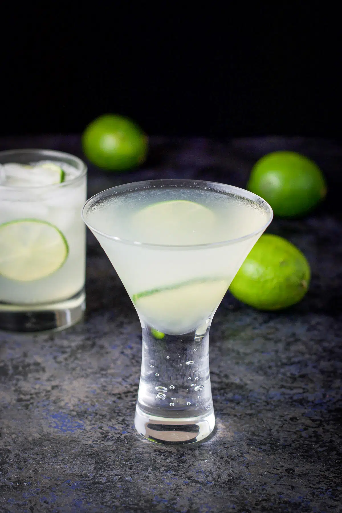 The martini glass filled with the lime drink with garnish and limes in the back