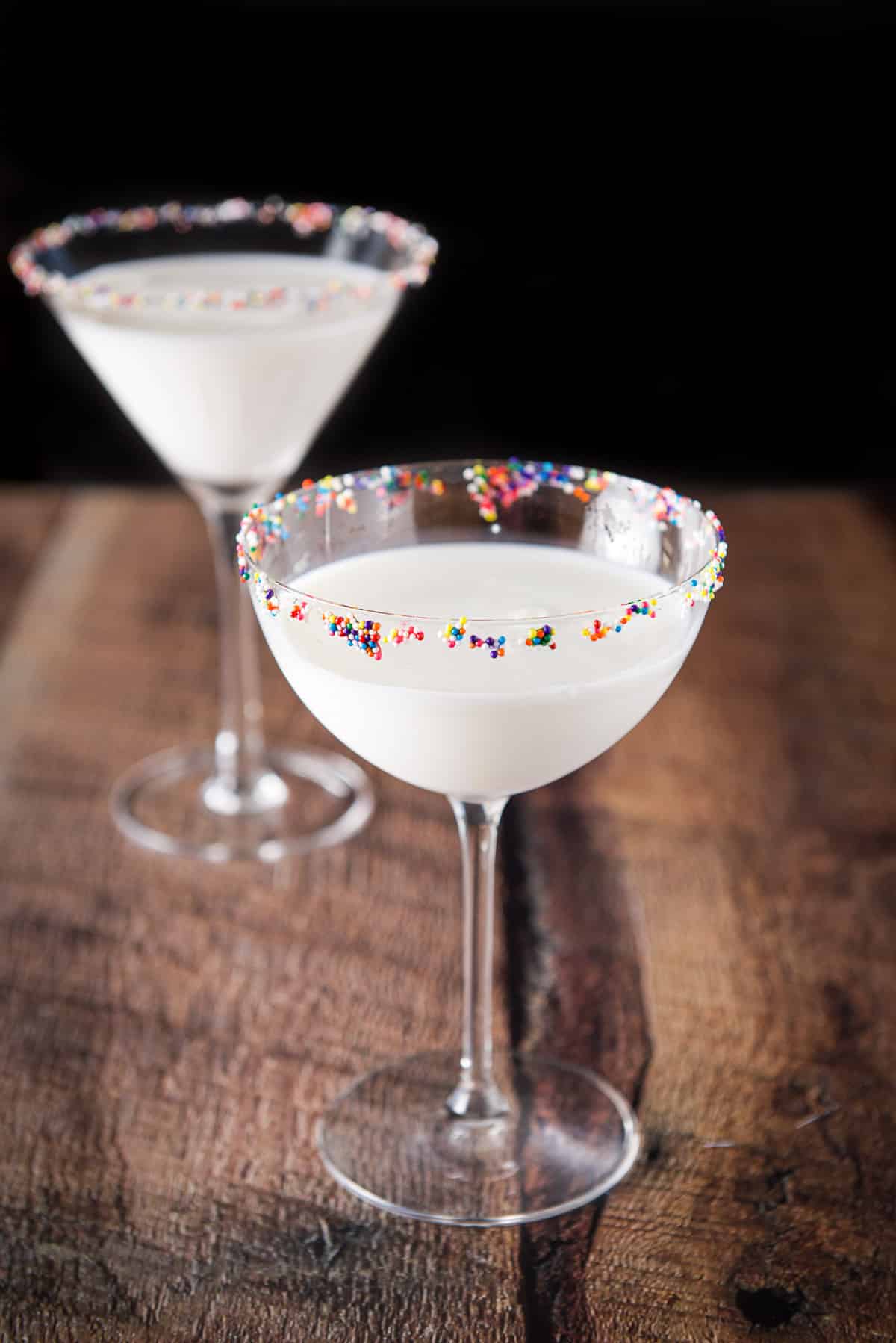 A bowl martini glass in front of a regular glass filled with a cream cocktail