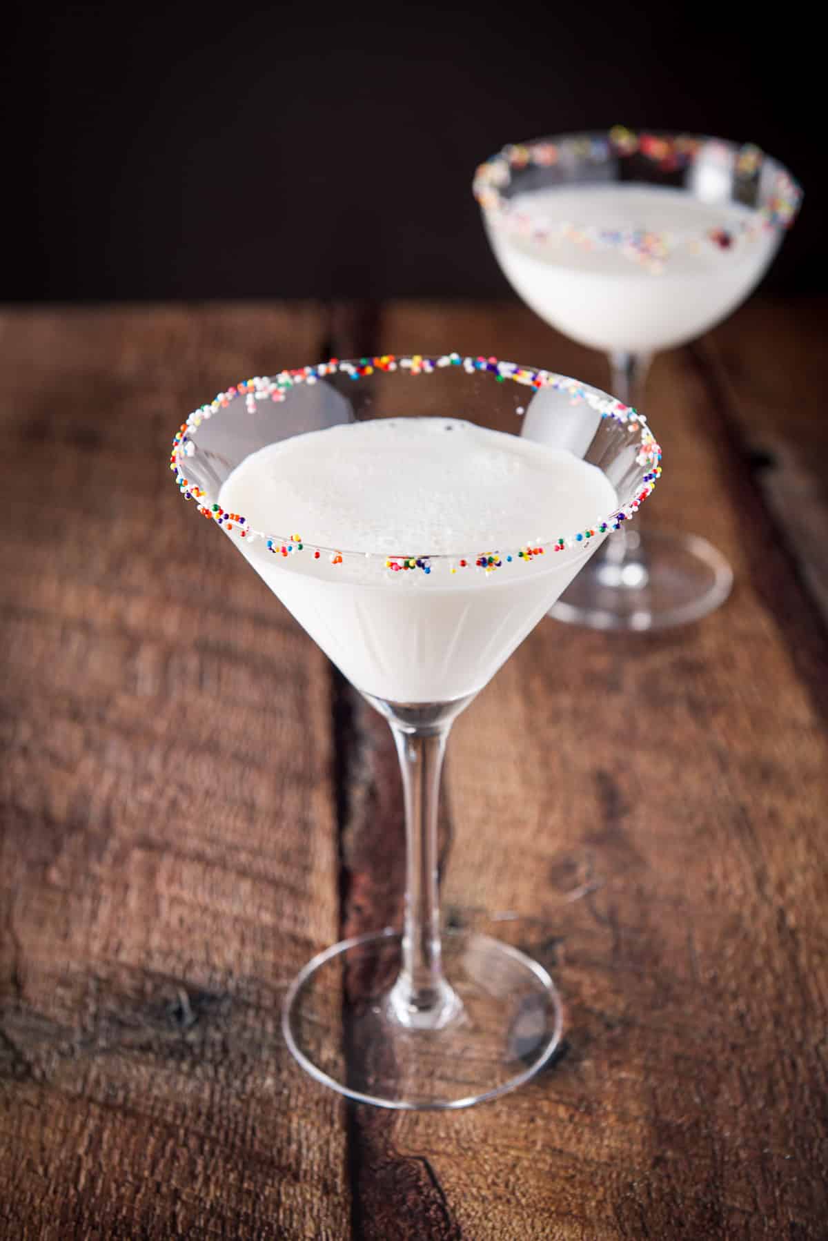 Two martini glasses with a cream cocktail and colored balls on the rim as garnish