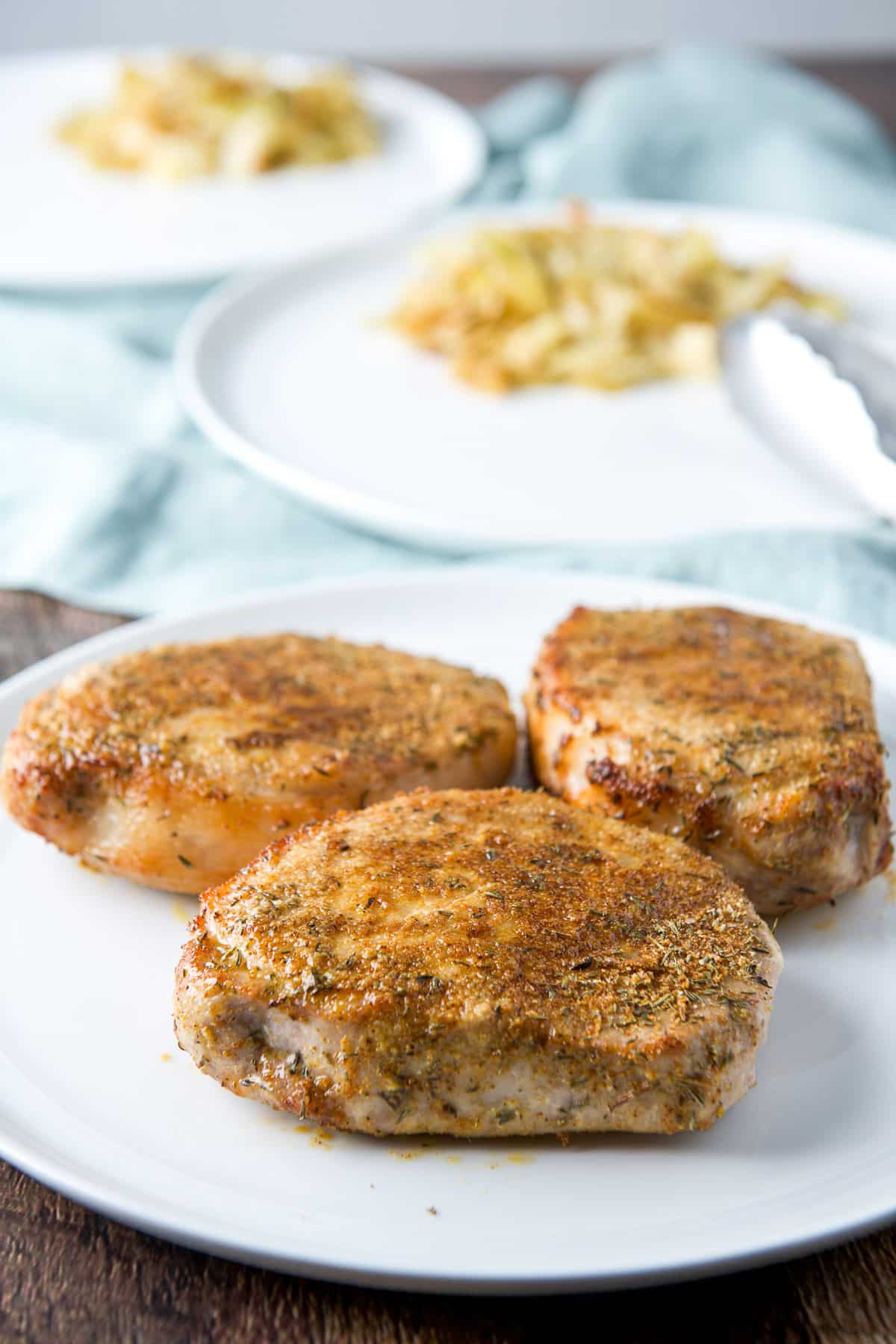 A plate with three pork chops on it with two plates in the back with vegetable on it