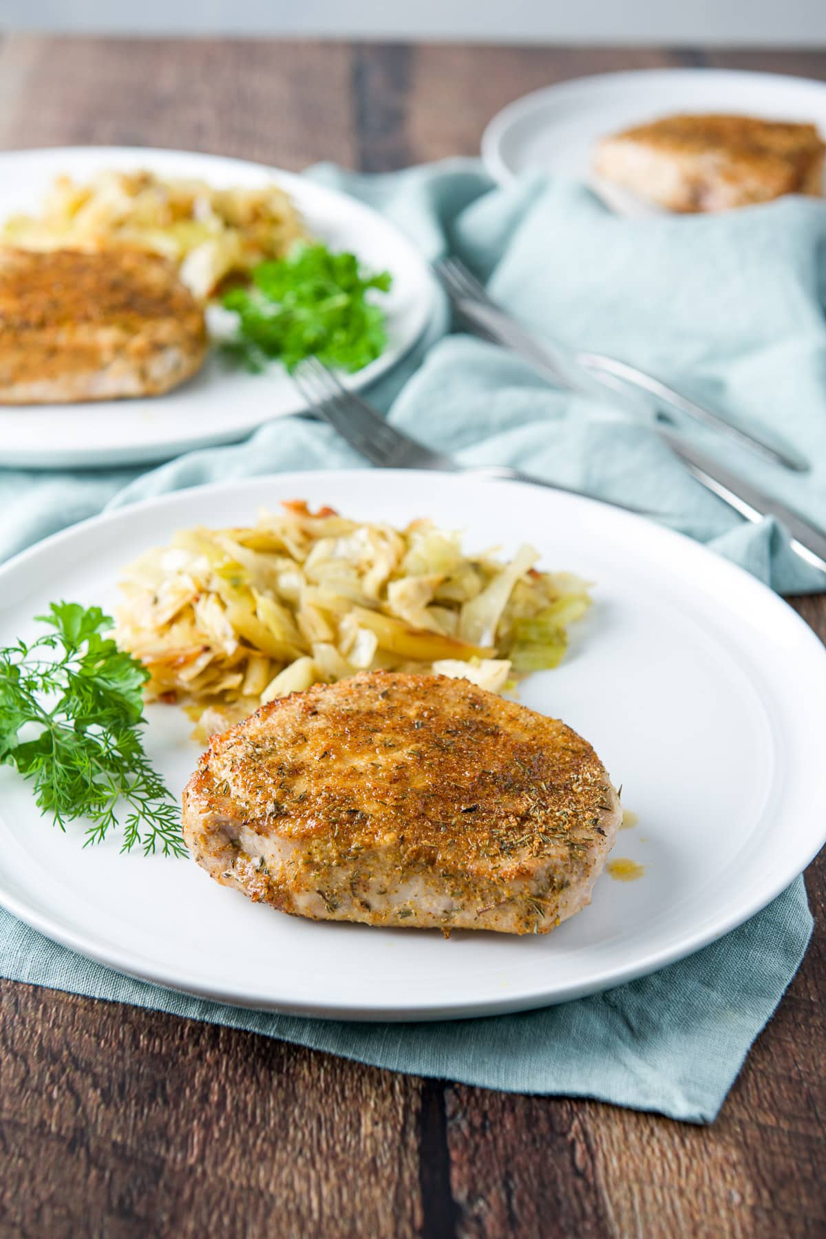 Two plates with pork chops, cabbage and herbs with a third chop in the back