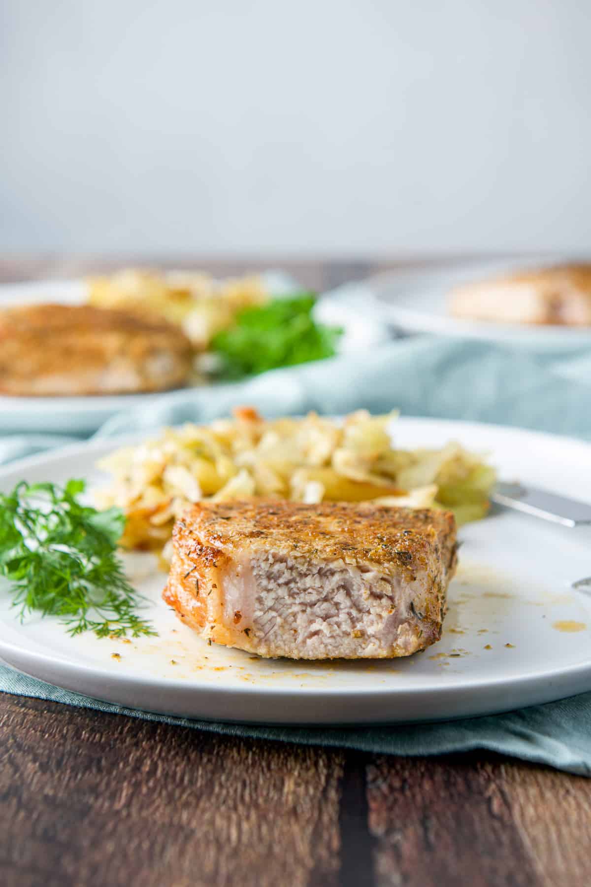 A pork chop with a slice taken out of it on the plate with herbs and a vegetable