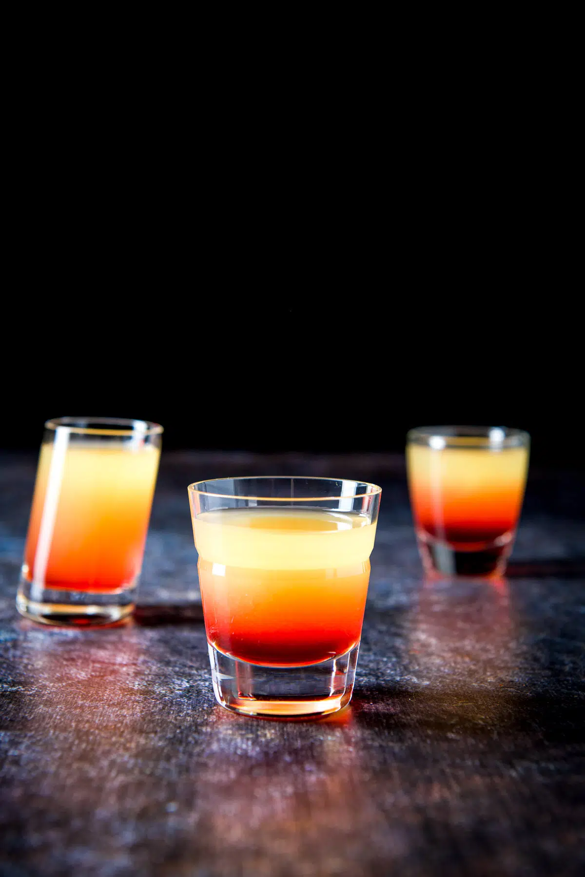 A beveled glass with the layered colorful orange red shot in front of two other glasses