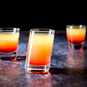 Tilted glass in front of two other glasses filled with the pineapple upside down shot