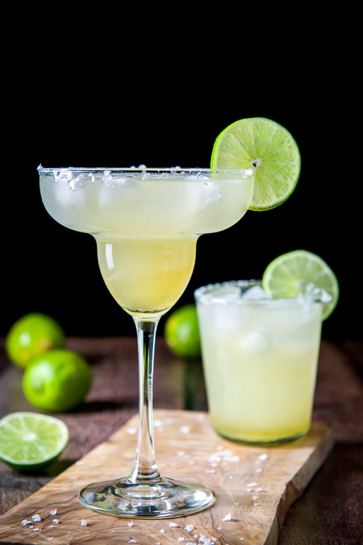 Classic margarita glass in front of a short glass with salt and lime in the back