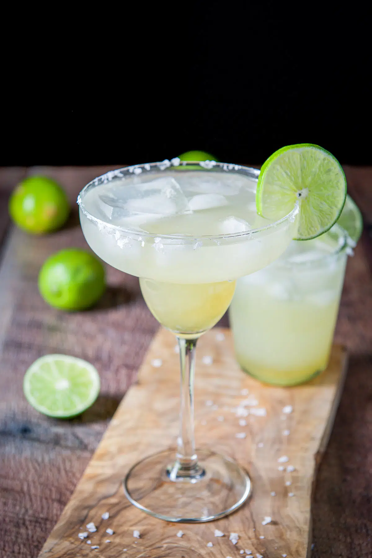 Two margaritas with salt on the rim and lime with salt strewn on the board