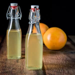 Square photo of two bottles of infused vodka with two grapefruit behind it