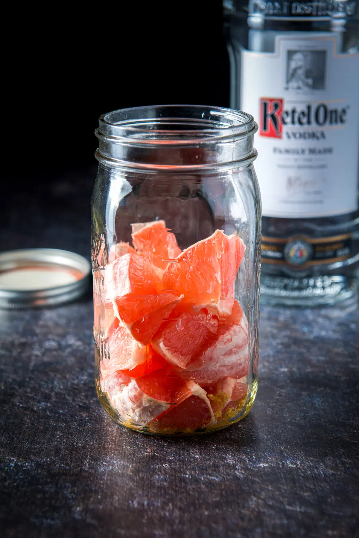A jar with the grapefruit pieces in it with vodka in the back