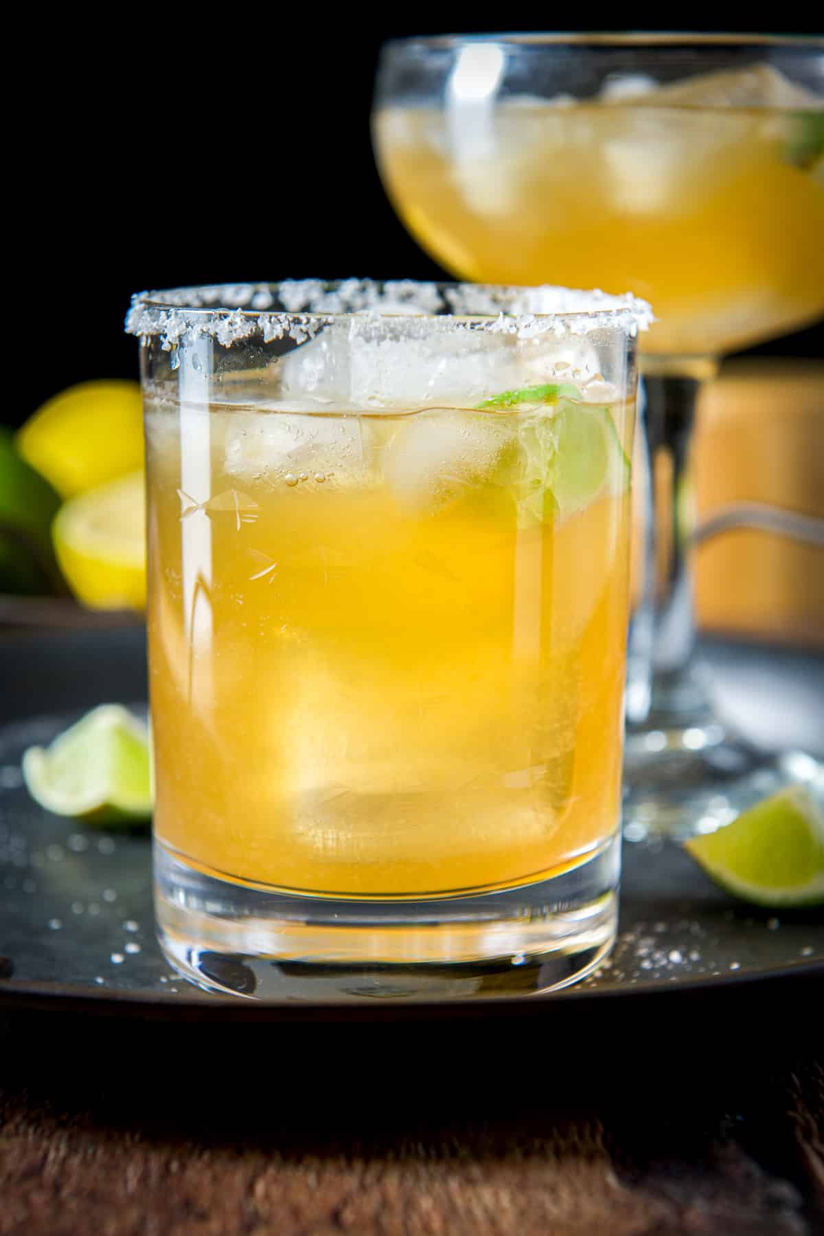 A salted glass filled with an amber margarita in front of a tall bowl glass