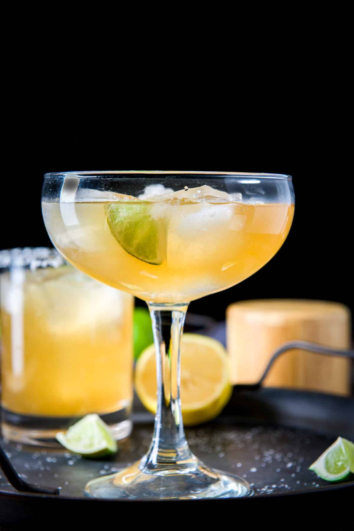 Vertical view of a bowl glass with amber liquid and lime in front of another glass