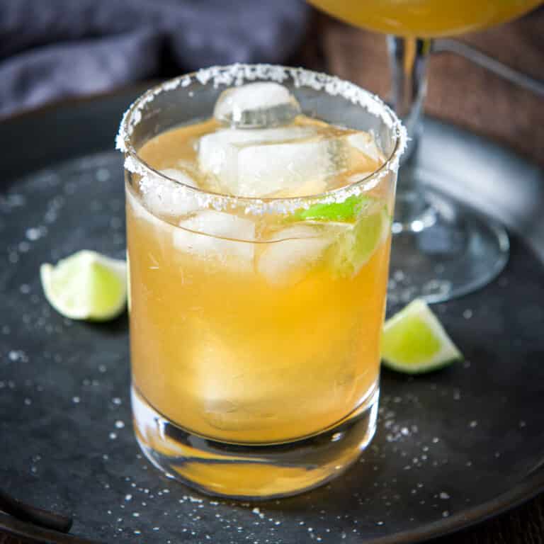 A salted glass with a margarita in it on a metal tray with lime wedges - square