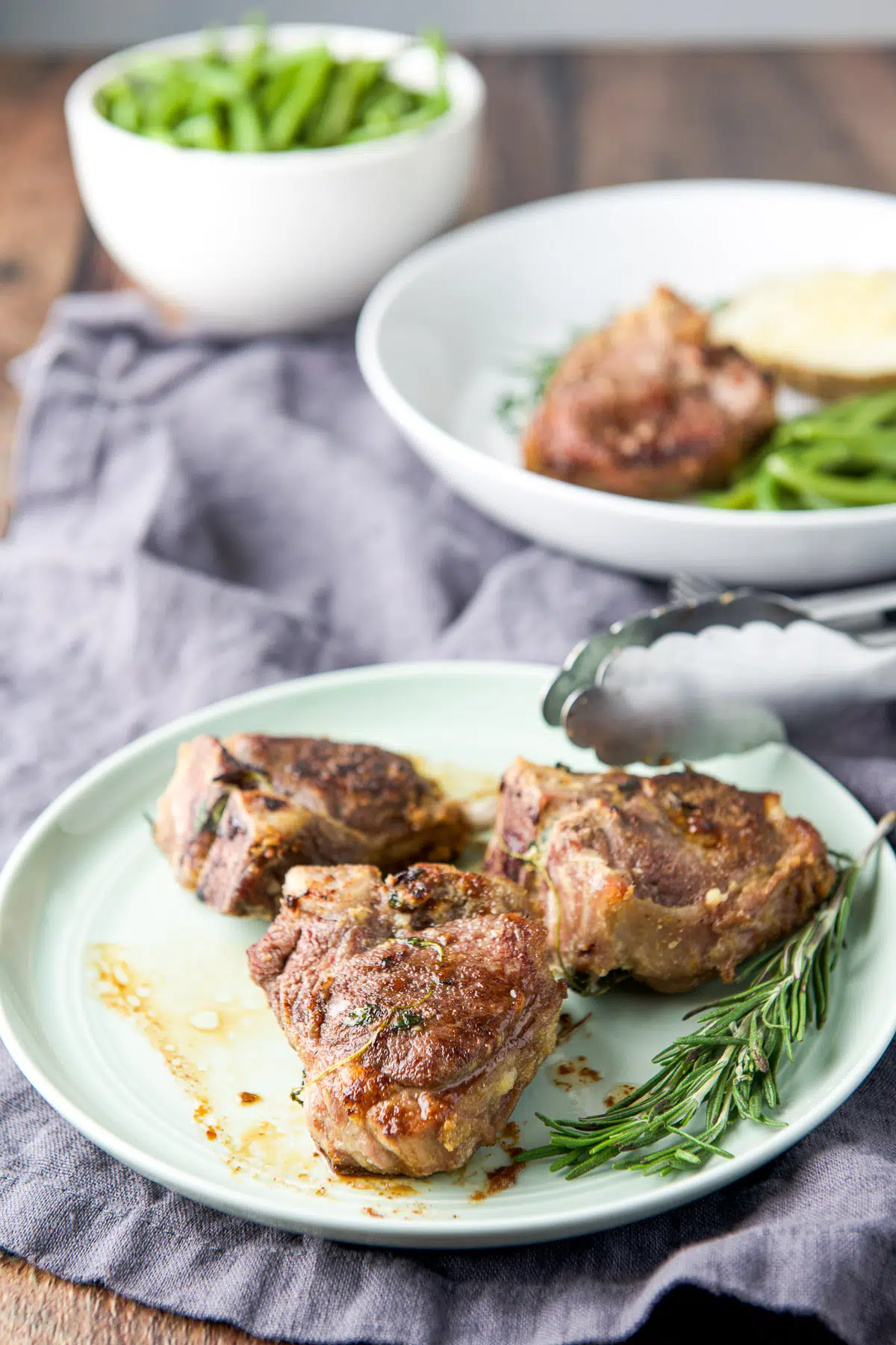 Three chops on a small green plate with fresh rosemary in front of a plate