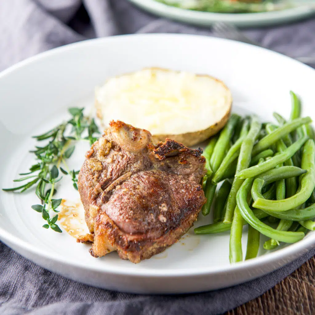 square photo of a lamb chop on a plate with green beans and half a potato