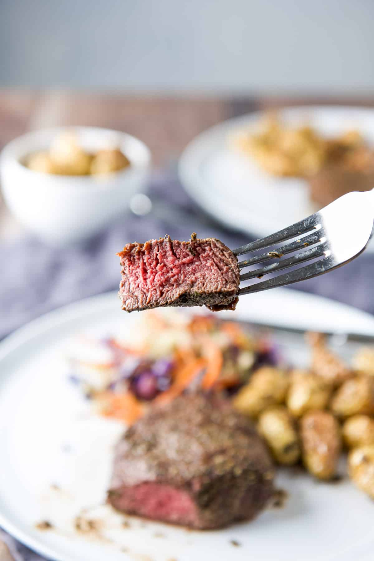 A fork with a piece of steak held over a white plate with the meal on it
