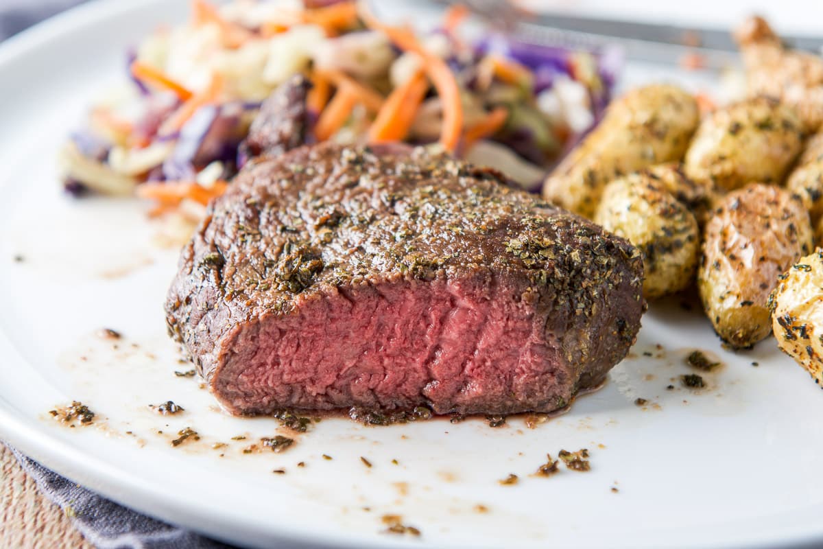 A cut into steak on a plate with potatoes and veggie - horizontal