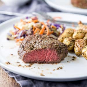 A white plate with a steak with a cut in it, with potatoes and veggies - square