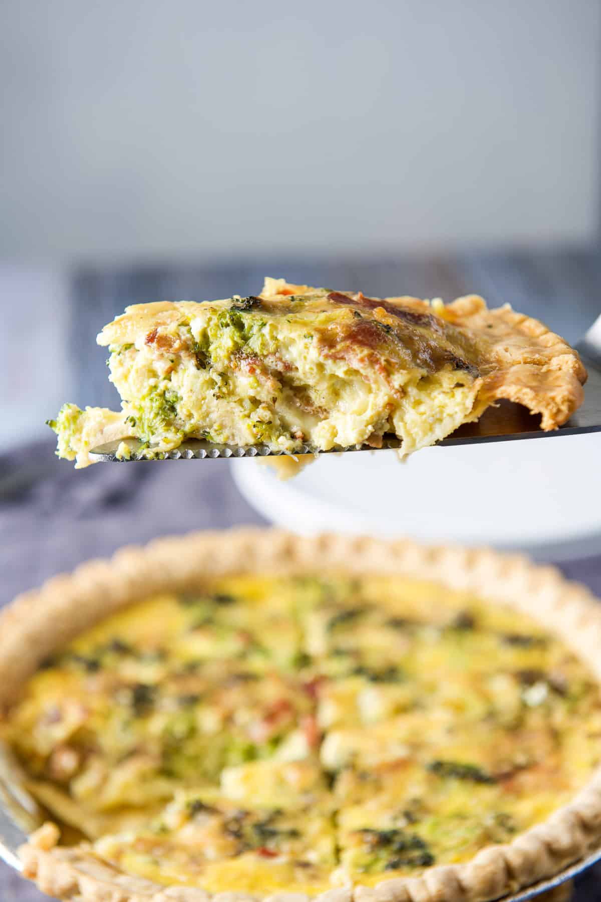 A slice of quiche on a server held over the pie