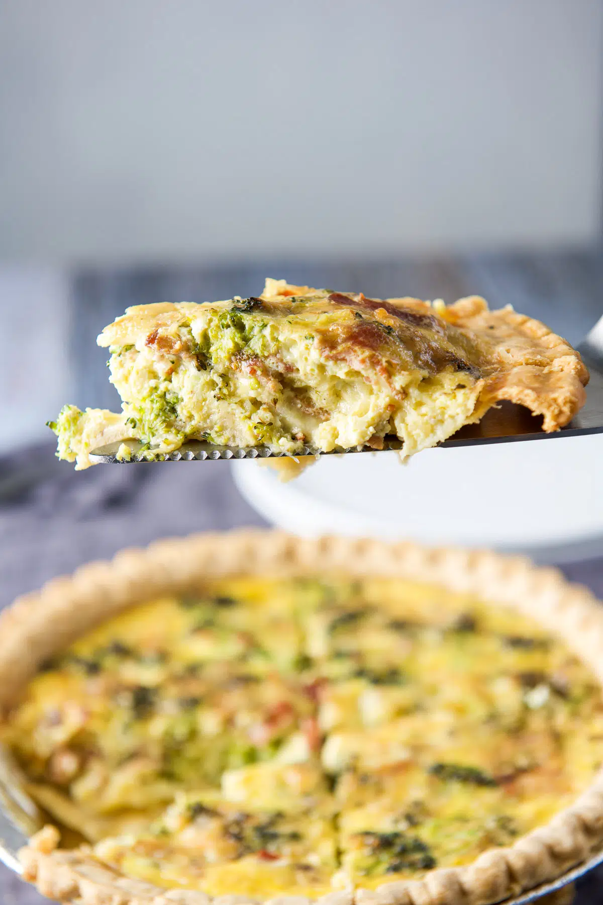 A slice of quiche on a server held over the pie