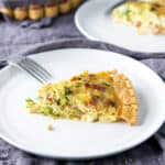 A piece of broccoli quiche on a white plate with a fork on the side - square