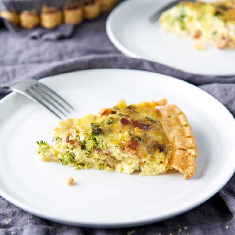 A piece of broccoli quiche on a white plate with a fork on the side - square