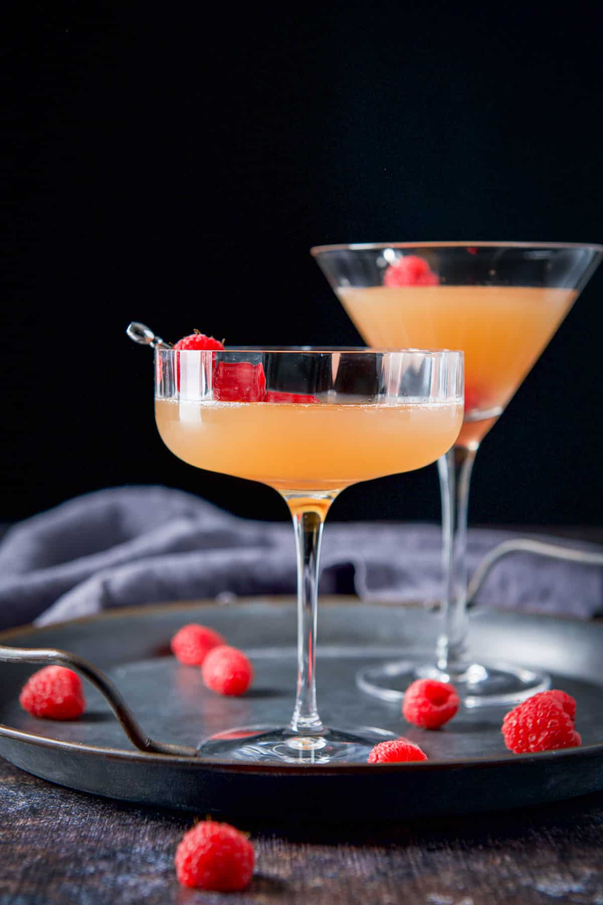 Vertical view of the two martini glasses filled with the French cocktail with raspberries as garnish and on the tray