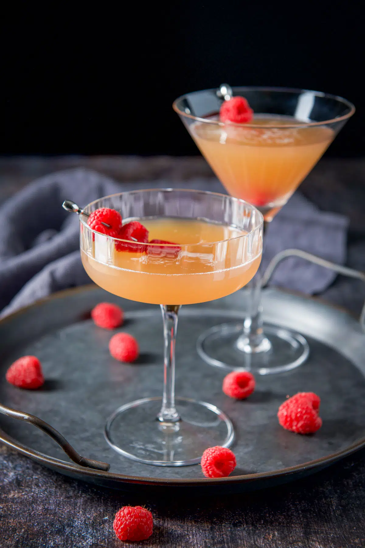 A coupe glass with an amber cocktail with raspberries as garnish
