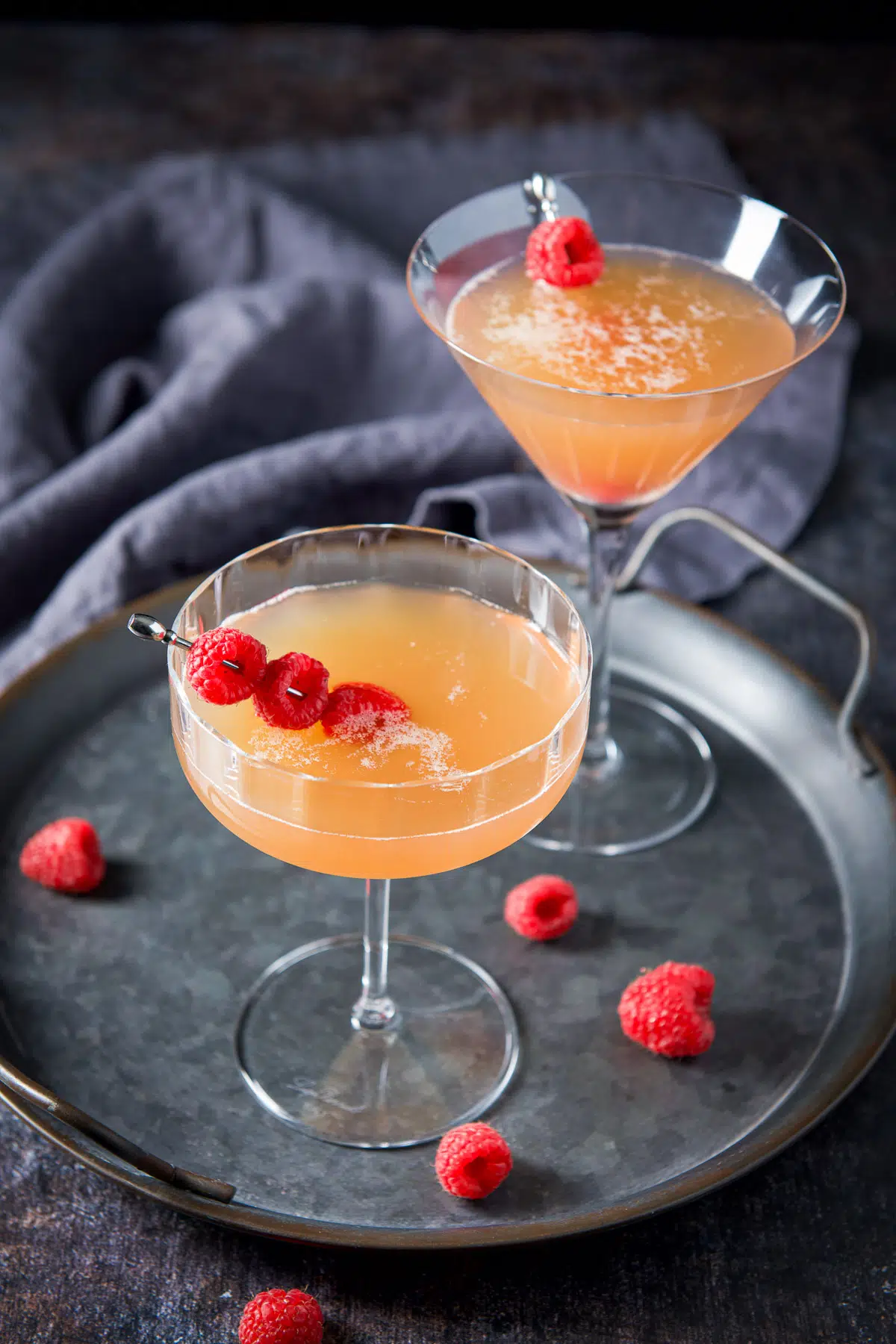 A metal tray with two martini's on it with raspberries as garnish