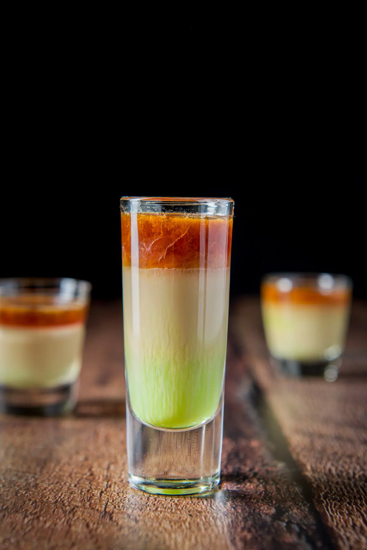 A tall shot glass with the layered shot in it. the colors are green, tan and brown