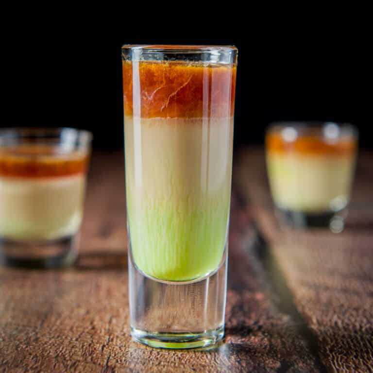 Square photo of a green, tan and brown shot in a tall glass