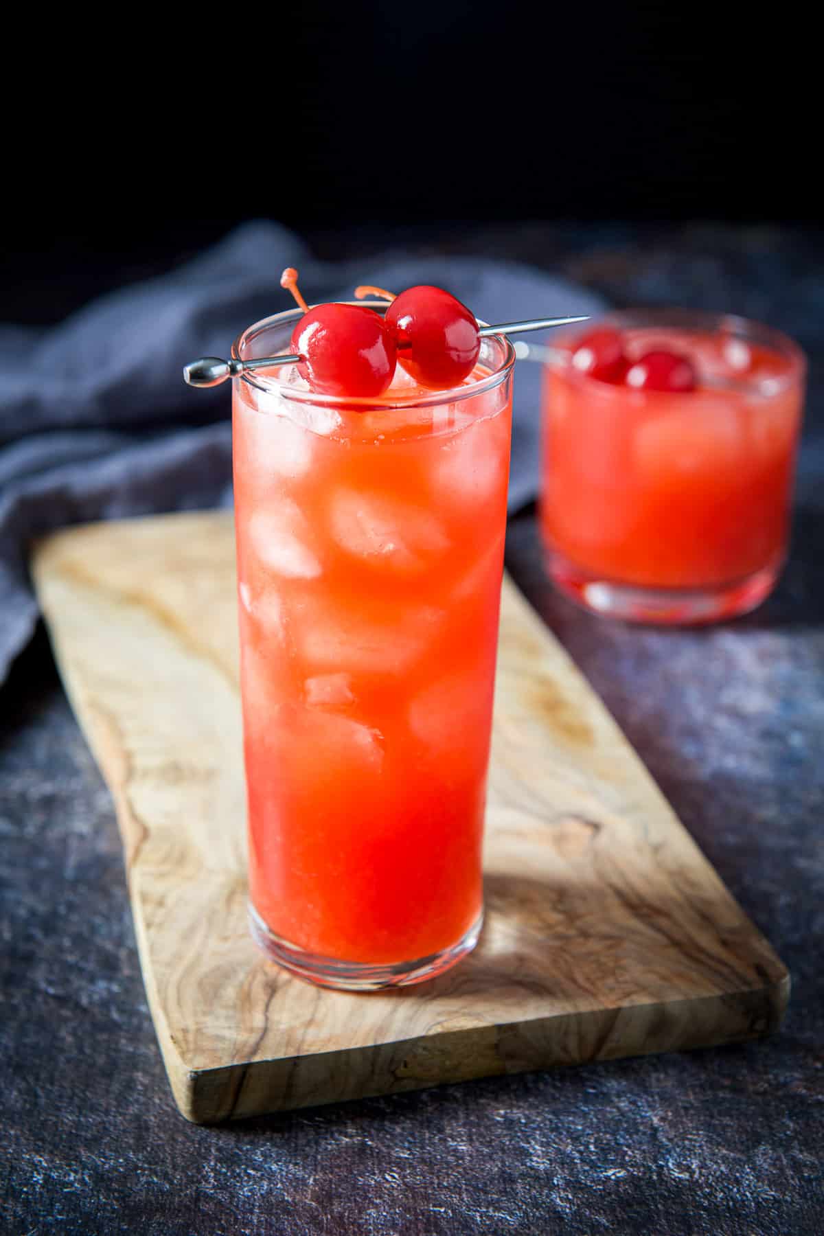 A tall glass filled with the Alabama slammer on a wooden board with the short glass off to the right