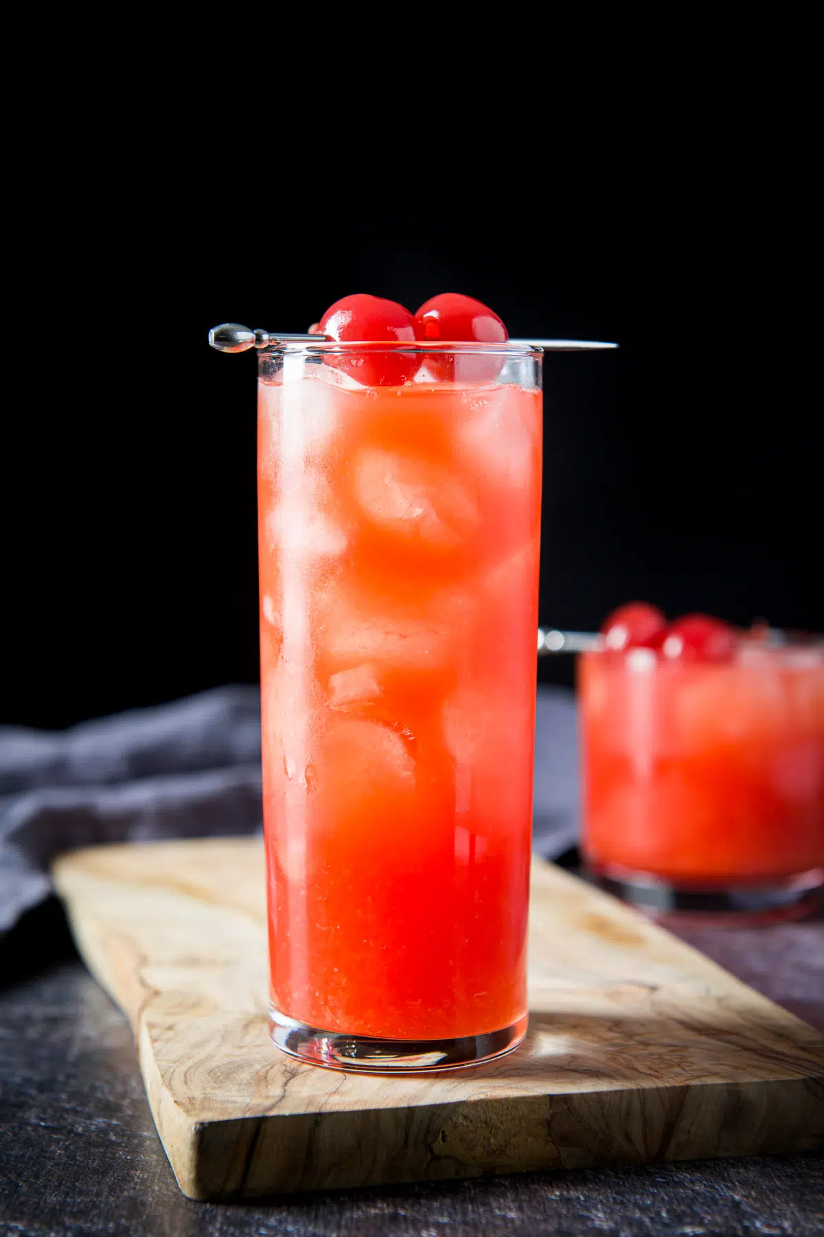 Vertical view of the tall glass filled with the cocktail with two cherries on a pick