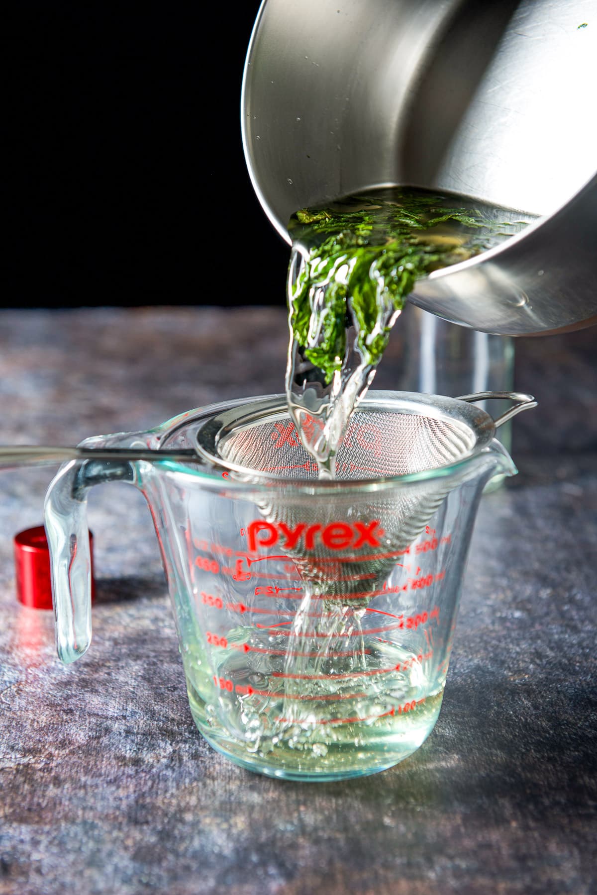 Pouring the mint water in a sieve over a measuring cup