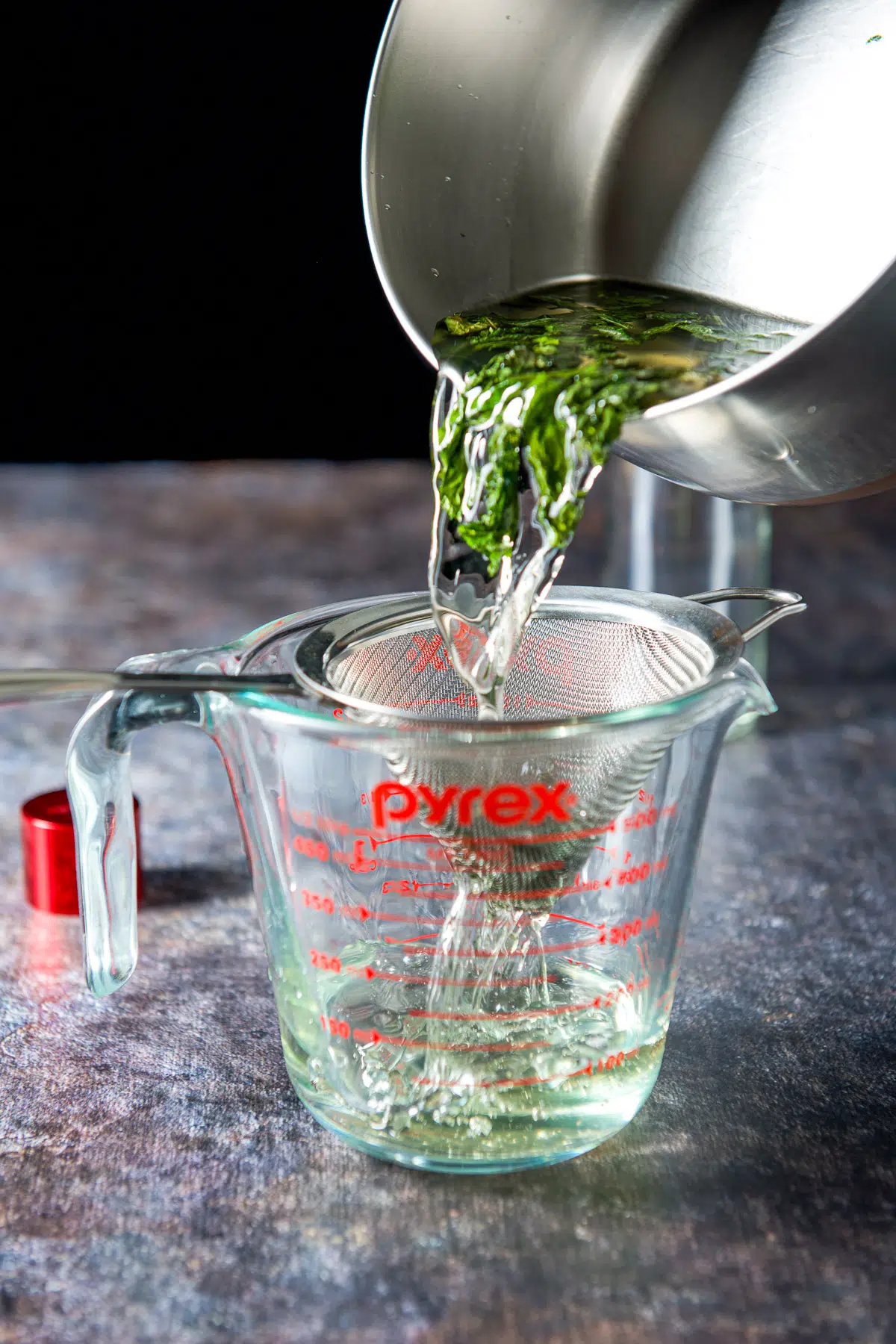 Pouring the mint water in a sieve over a measuring cup