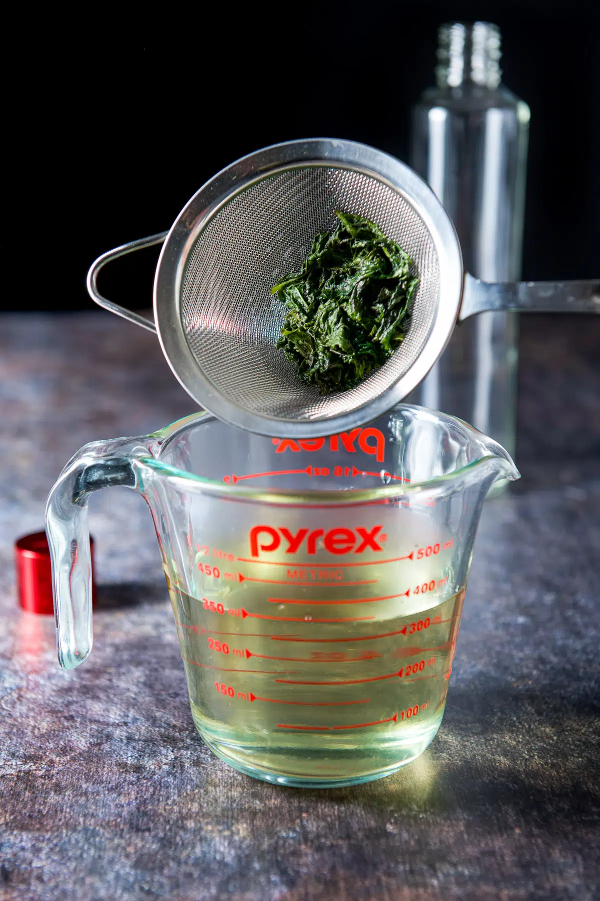 The sieve with the mint over the cup measure with the liquid in it