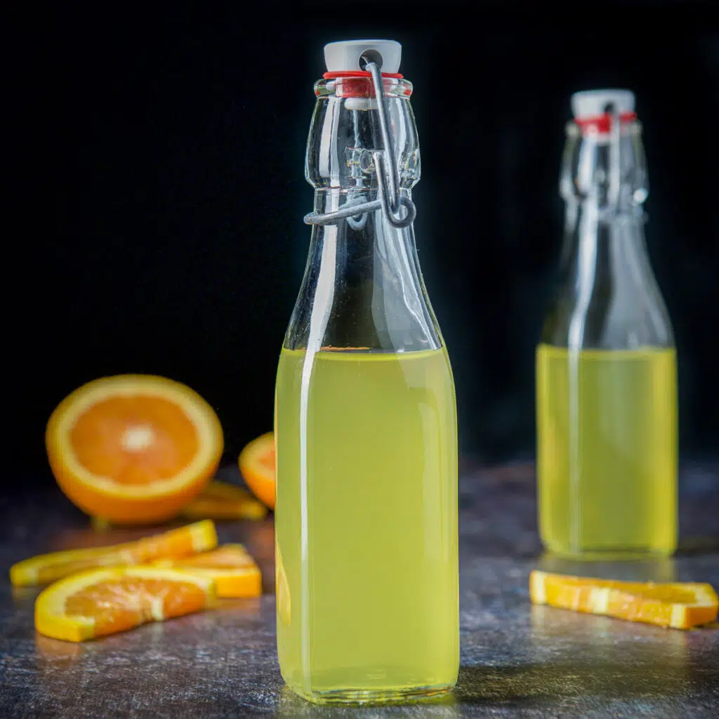 Vertical view of two small bottles of vodka with oranges in the back - square