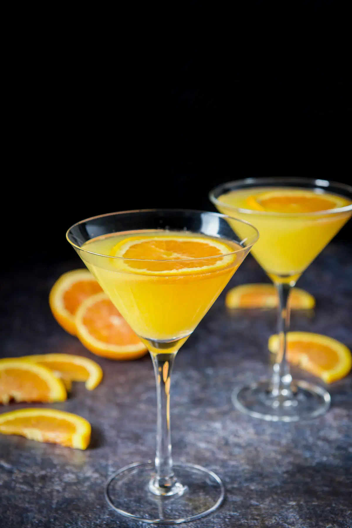 Two martini glasses with the orange drink and orange slices floating as garnish