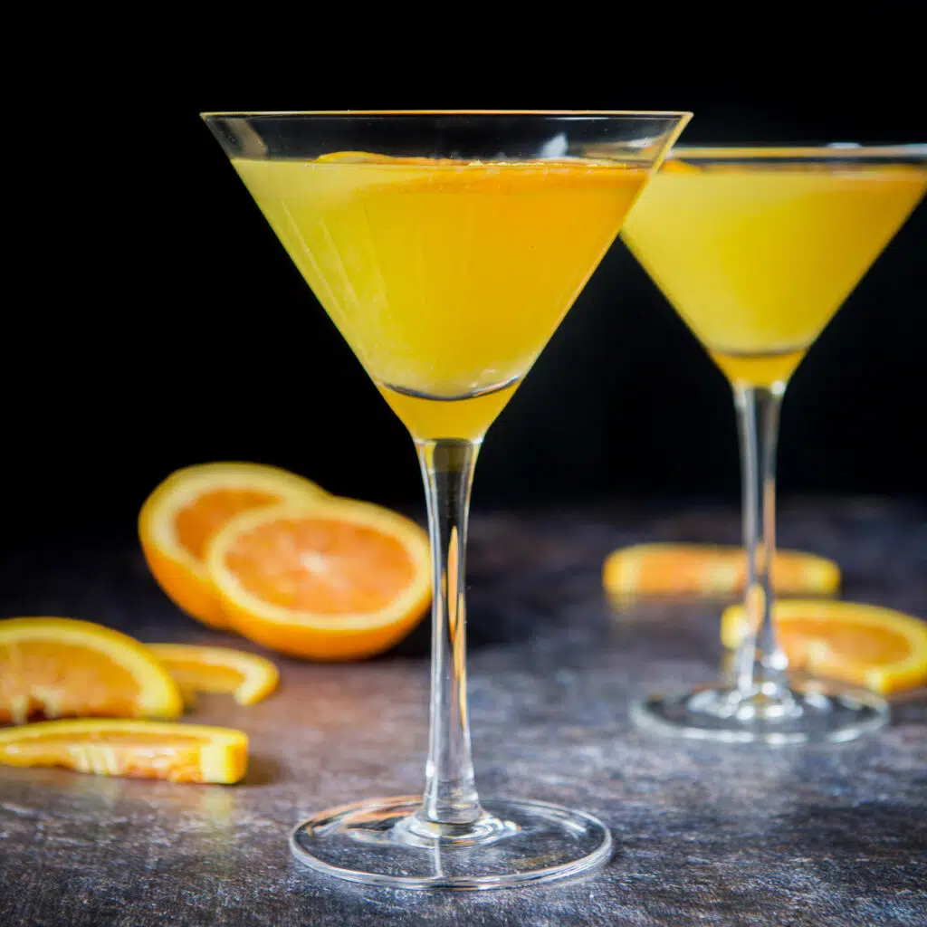 Two orange martinis in classic glasses with sliced oranges on the table