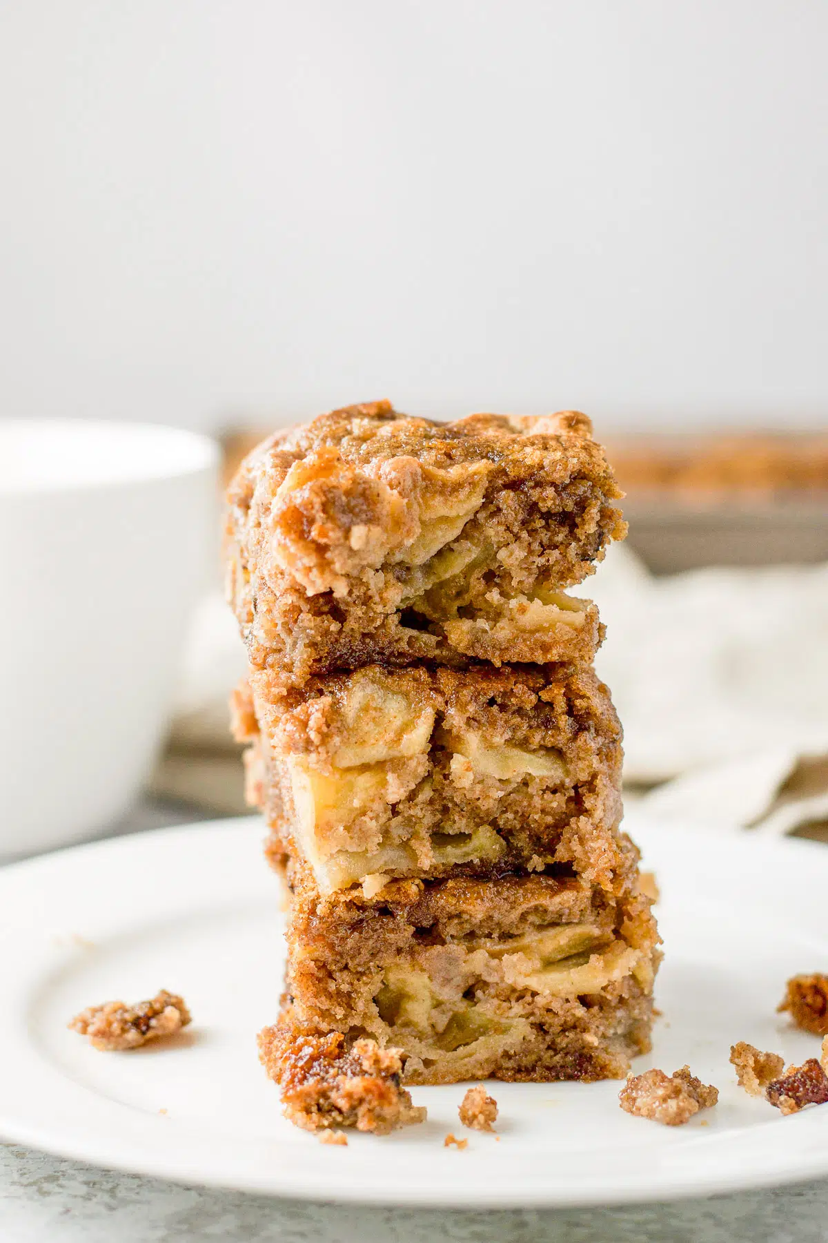 Three pieces of apple cake in a tower with a coffee cup in the back