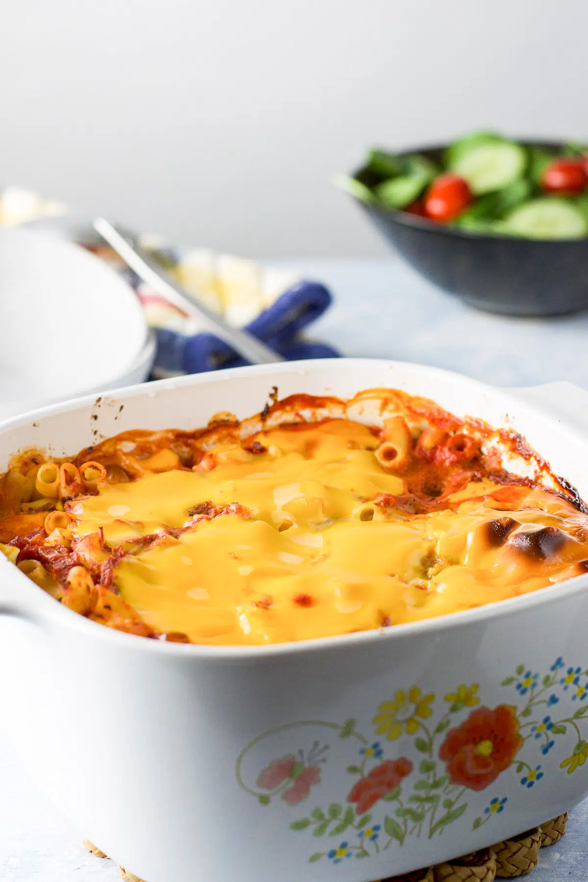 A casserole dish with cheese melted on pasta with a salad in the back