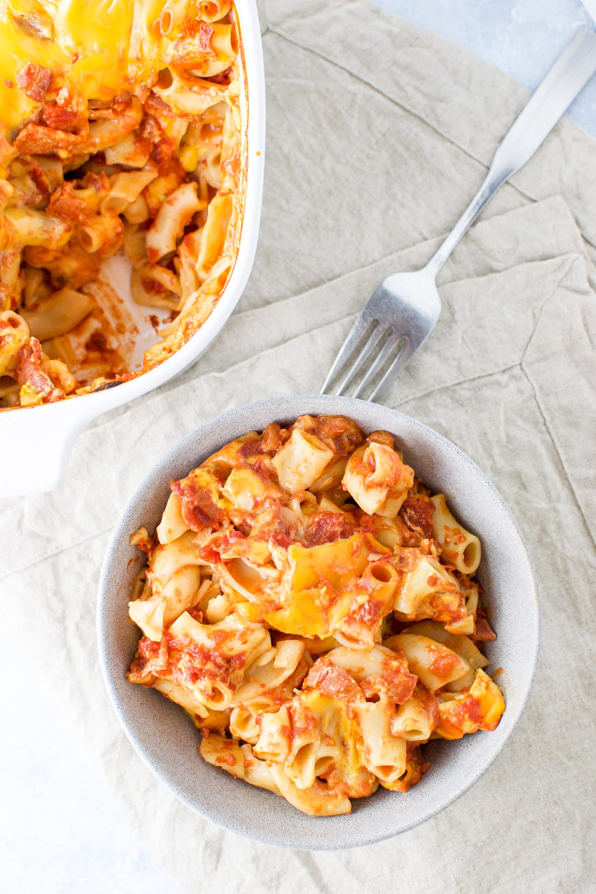 Overhead view of the bowl of cheesy pasta with a fork and casserole dish in the back