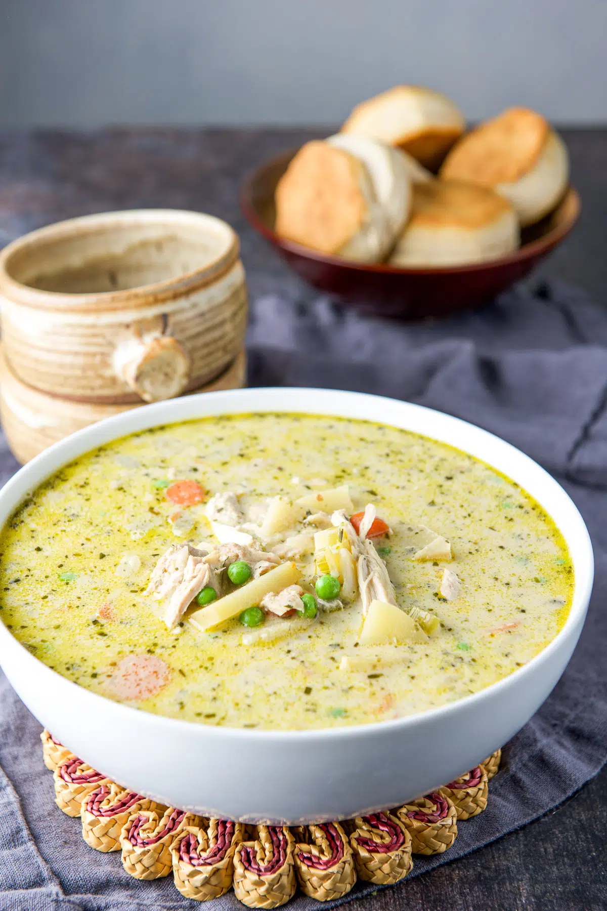 Large white bowl filled with the creamy chicken soup with crocks and biscuits in back