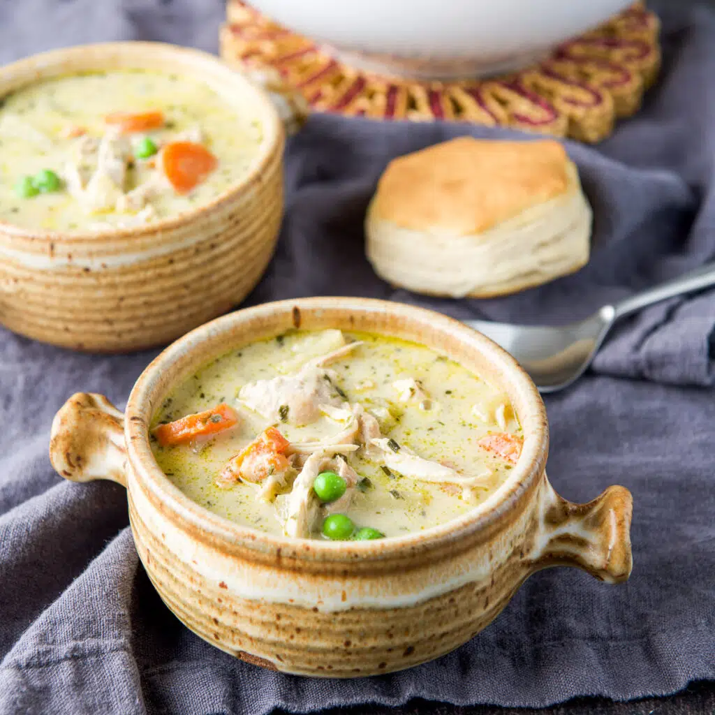 Two crocks frilled with the chicken pot pie soup with a biscuit on the table