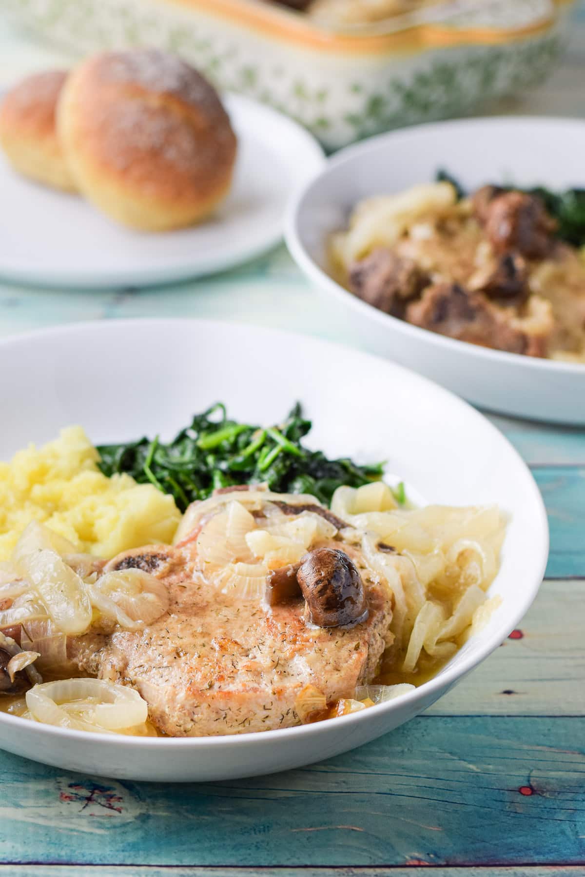 A white plate with a pork chop, potato, onion and spinach on it