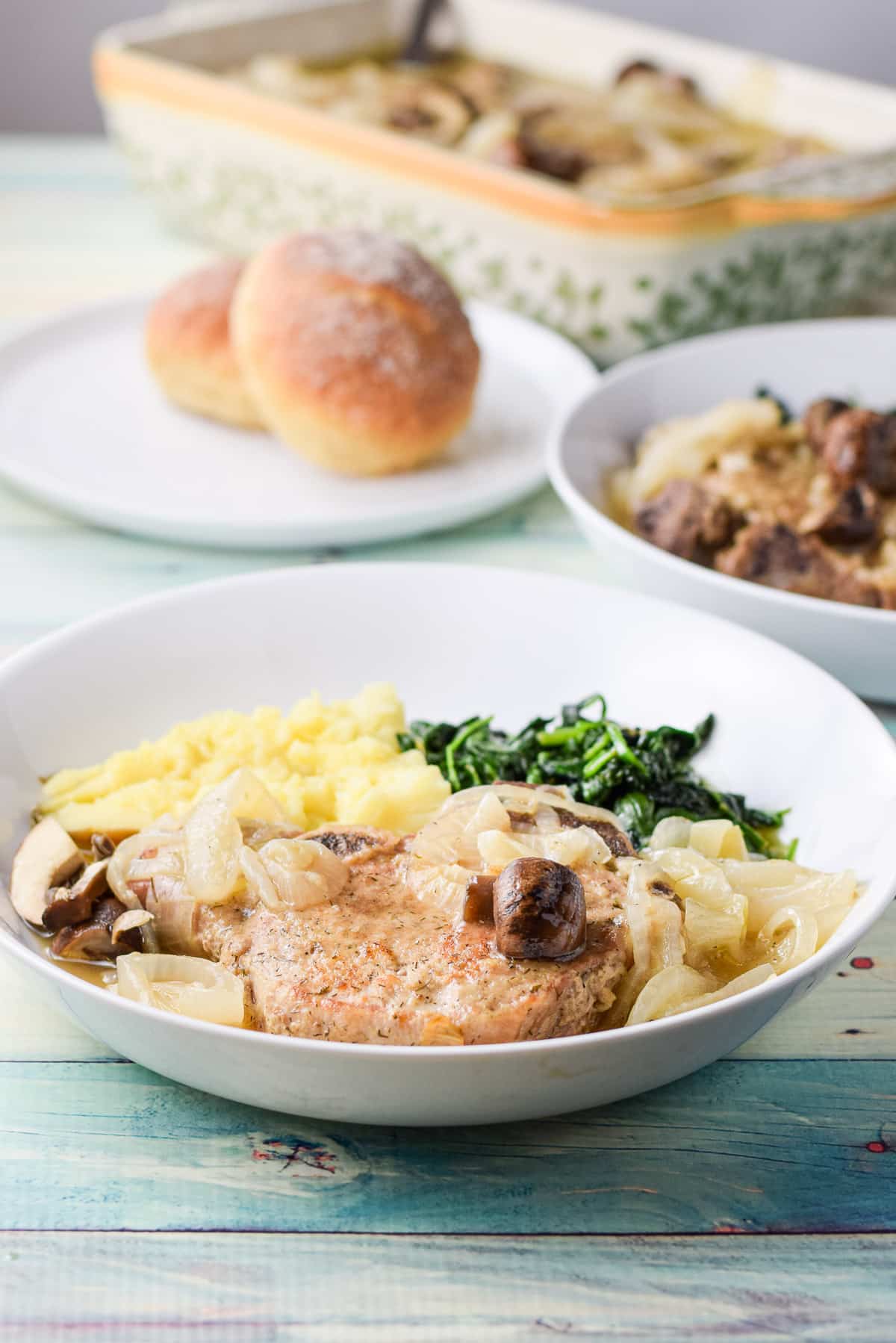 Pork chops in two white dishes with rolls and a casserole dish with the meat in back