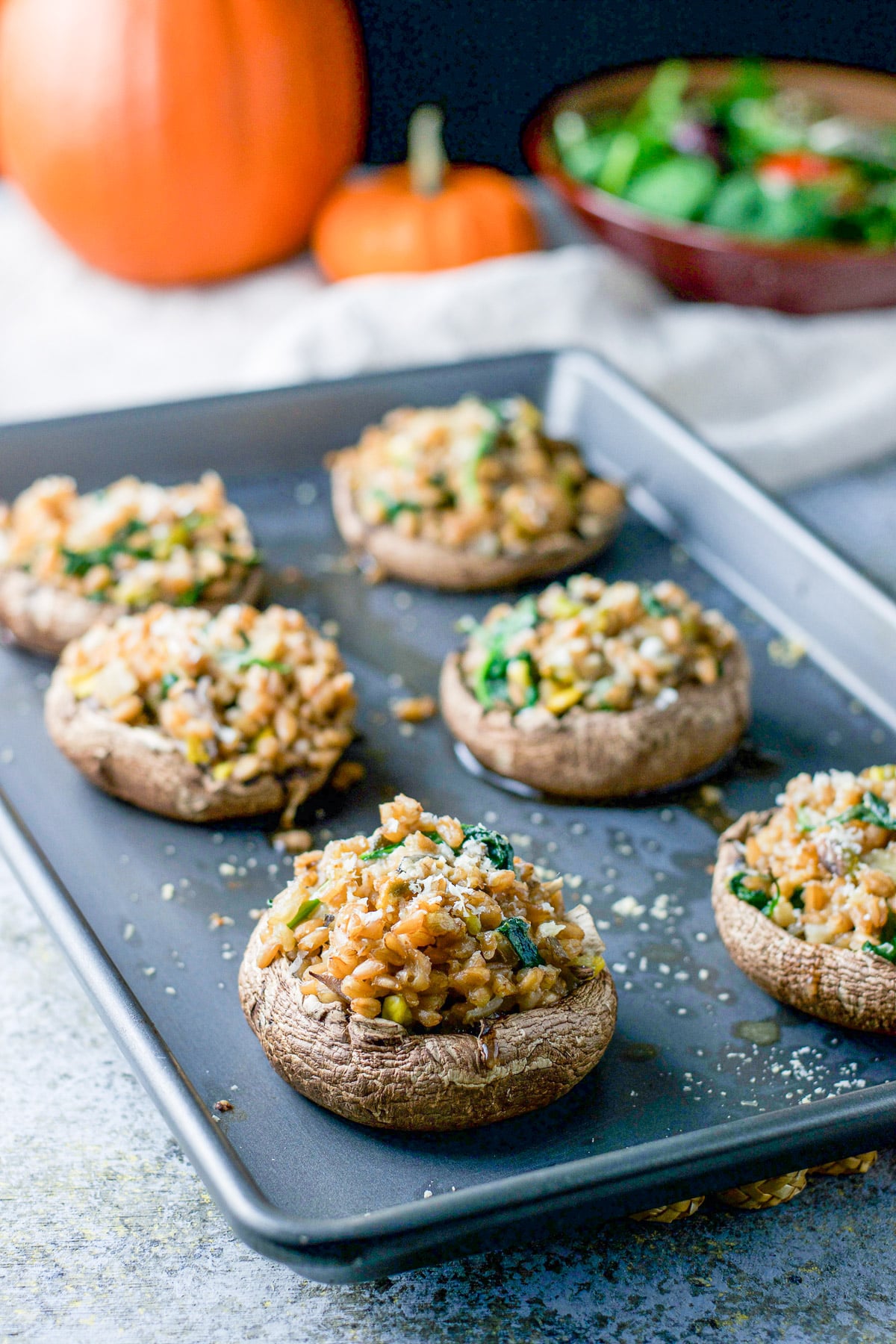 Cooked mushroom caps on a pan with a salad and pumpkins in the back